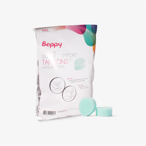 A product photograph of the Beppy Soft Comfort Tampons Dry. The white plastic packaging features the pink Beppy logo and colorful abstract graphics. Two mint green sponges are displayed in front of the bag. The package includes diagrams showing "Easy In" and "Easy Out" instructions for stringless use.