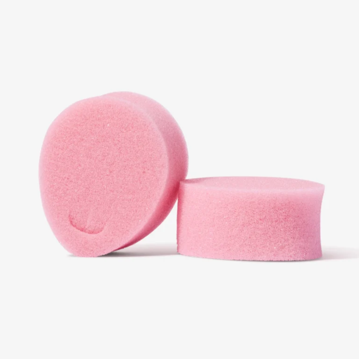 A studio shot featuring two pink sponge tampons. One is standing upright on its side, showing the removal loop indentation, while the other lies flat next to it, highlighting its cylindrical height and soft texture.