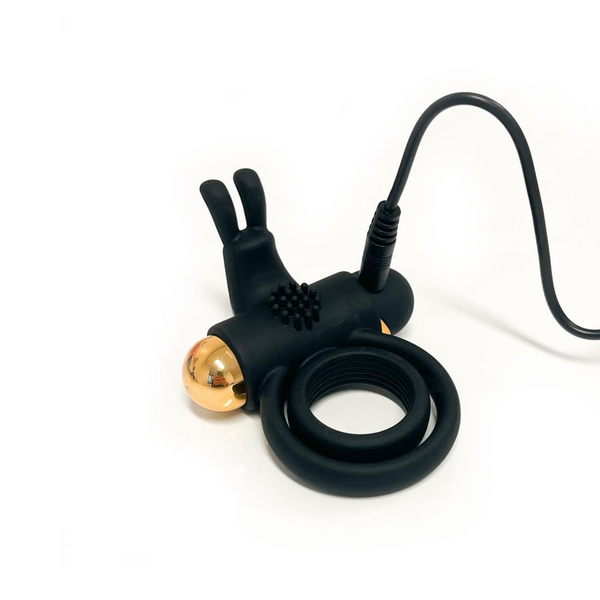 Black vibrating ring shown with its charging cable plugged into the end of the device.