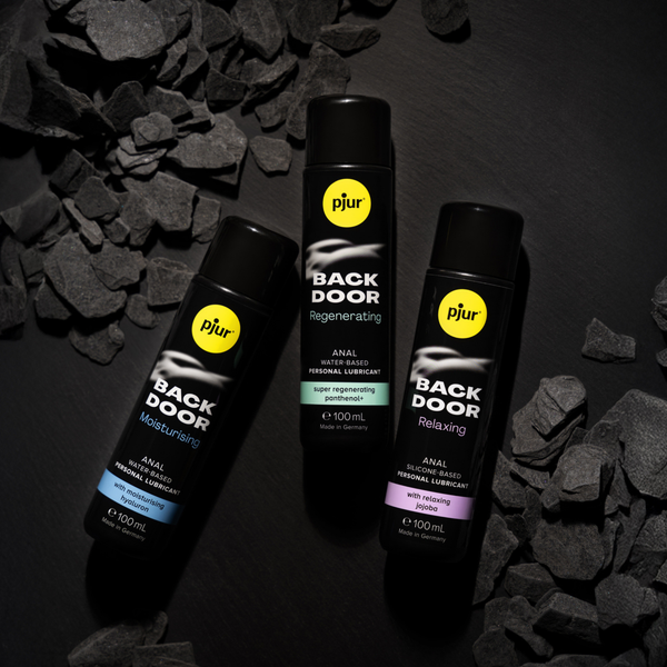 Three black bottles of pjur BACK DOOR lubricant arranged in a triangular formation on a sleek, dark, polished wooden surface.