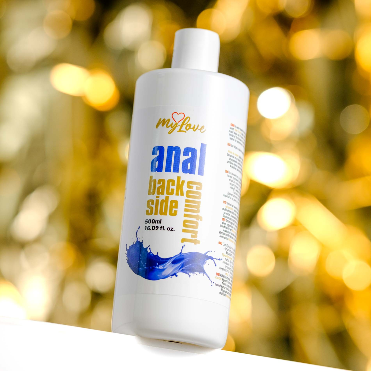 Front view of the 500 ml MyLove Anal Back Side Comfort bottle set against a warm, heavily blurred golden bokeh lighting background.