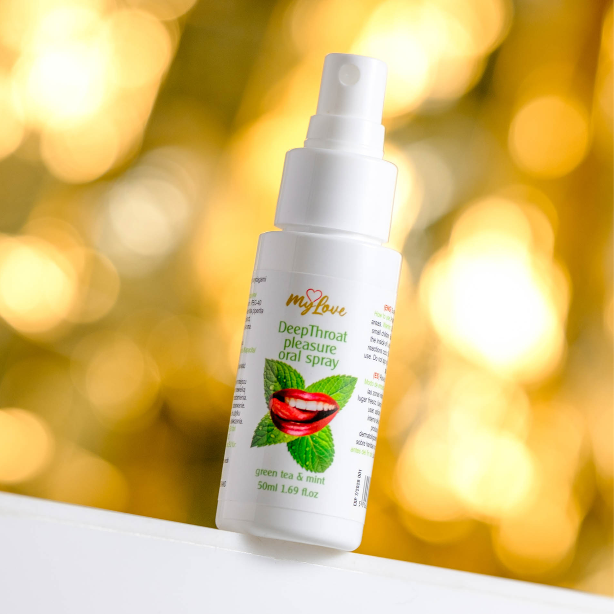 Front view of the 50 ml MyLove Deep Throat Pleasure Oral Spray bottle set against a warm, heavily blurred golden bokeh lighting background.