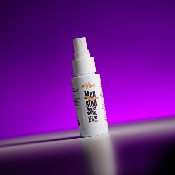 Front view of the 50 ml MyLove Men Stud Comfort Delay Med Spray bottle, angled slightly on a white surface against a vibrant purple backlit background.