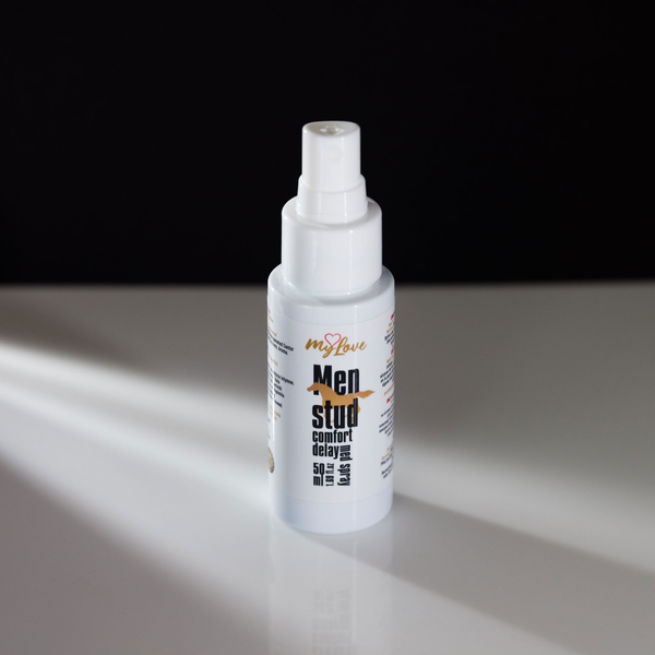 Front-angle view of the 50 ml MyLove Men Stud Comfort Delay Med Spray bottle standing on a white reflective surface against a solid black backdrop with soft side lighting.
