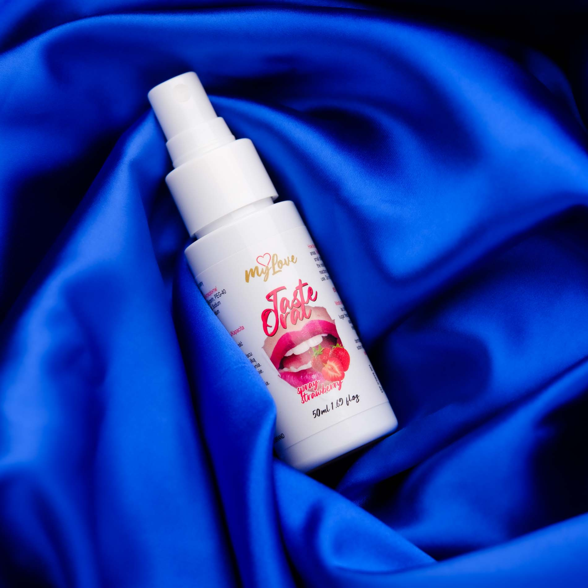 The 50 ml bottle of MyLove Taste Oral Spray in Strawberry flavor rests diagonally on draped, rich royal blue satin fabric.