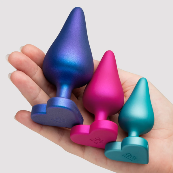 Scale view showing an open palm holding all three heart-based silicone plugs (blue, pink, and teal) to compare their relative sizes.