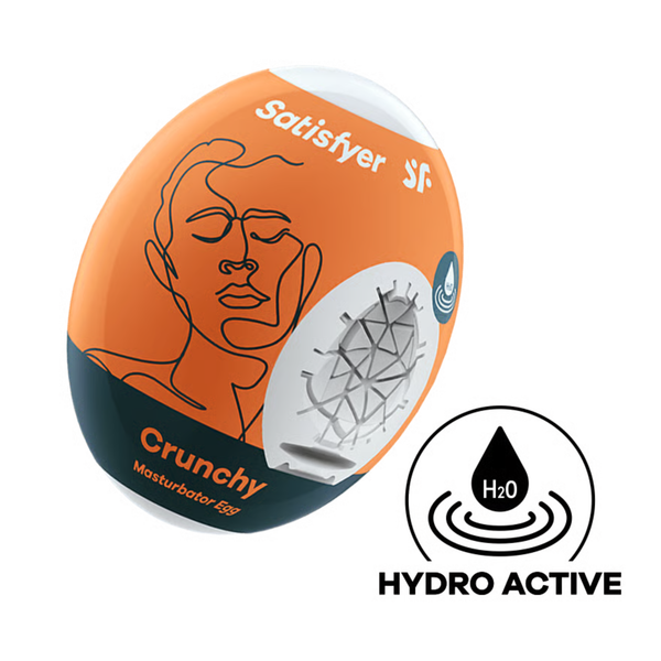 Studio product shot of the orange and dark slate Satisfyer Crunchy Masturbator Egg packaging, displaying a cutaway to the geometrically textured white inner sleeve and a circular "Hydro Active" icon below.