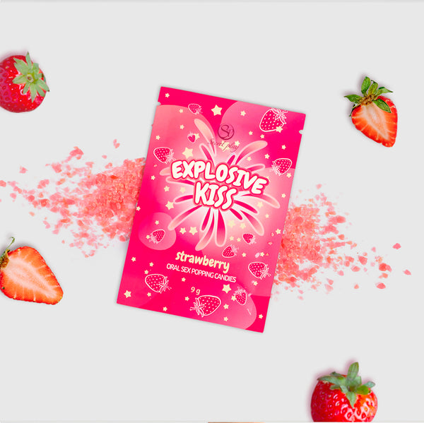 Pink packaging of 'Explosive Kiss' strawberry-flavored product with scattered pink powder and strawberries on a white background.
