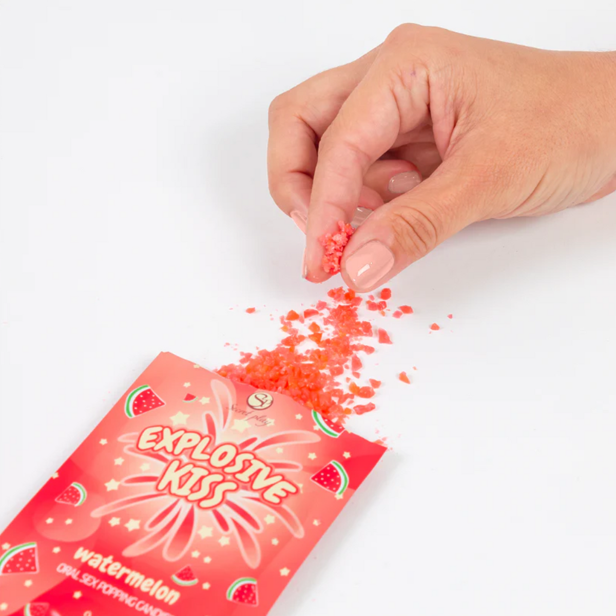 Red packaging of 'Explosive Kiss' candy with a hand sprinkling red powder on a white background