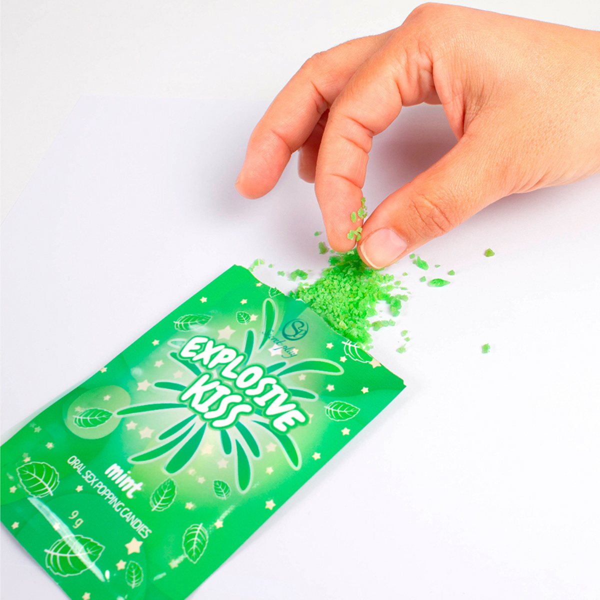Green packaging of 'Explosive Kiss' candy with a hand sprinkling green powder on a white background