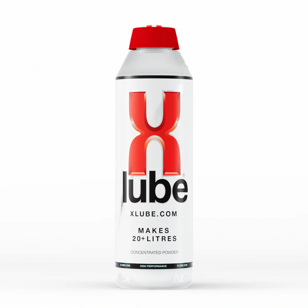 A vertical shot of a clear plastic bottle of X Lube powder lubricant in the white background. The bottle has a red cap and is primarily white with red and black text. The large red "X" and black "lube" logo is prominent in the center. Smaller text below the logo reads "Xlube.com" and "MAKES 20+ LITRES / CONCENTRATED POWDER".
