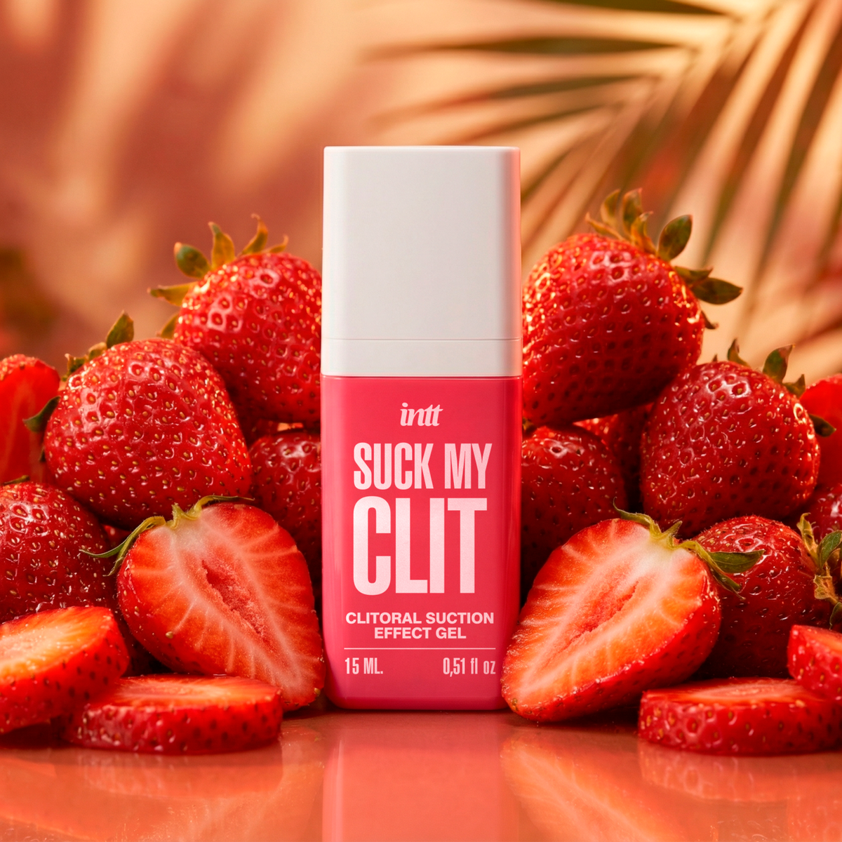 A pink and white bottle of the intt Suck My Clit Wild Strawberry clitoral suction gel stands upright, completely surrounded by a dense pile of whole and sliced fresh strawberries under warm lighting.
